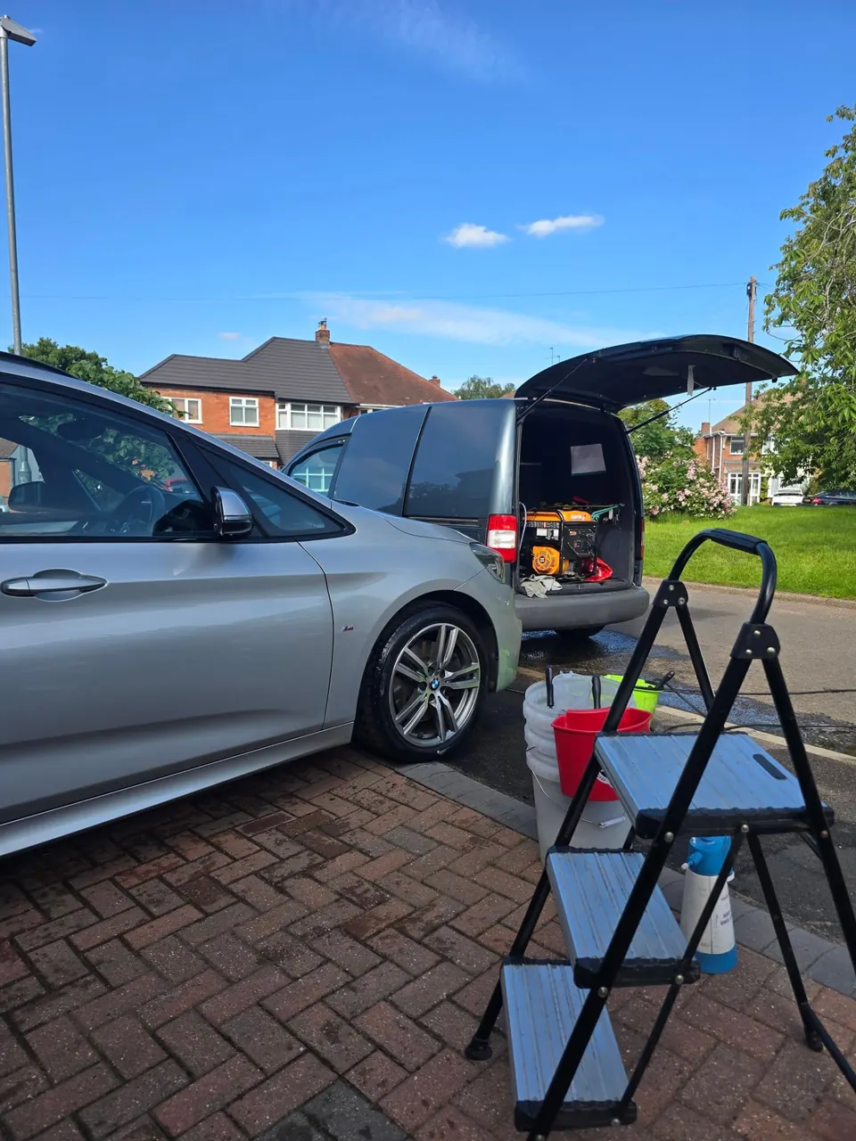 Silver BMW 2 Series on a driveway set up for a Sunday valet with buckets, a step ladder and the RM van behind