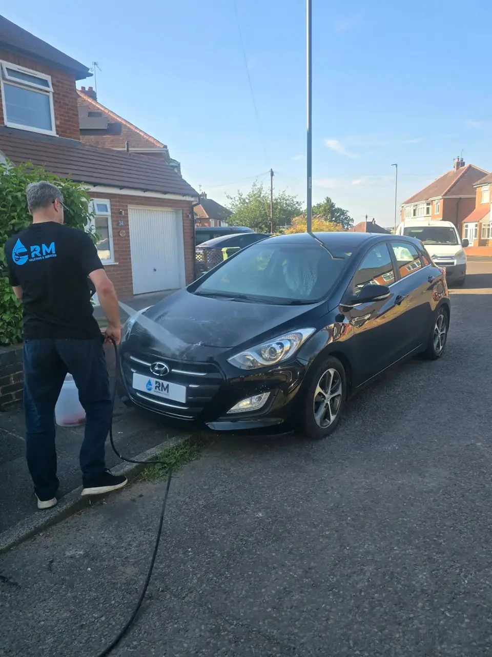 Riyaz rinsing the bonnet of a black Hyundai i30 on a driveway