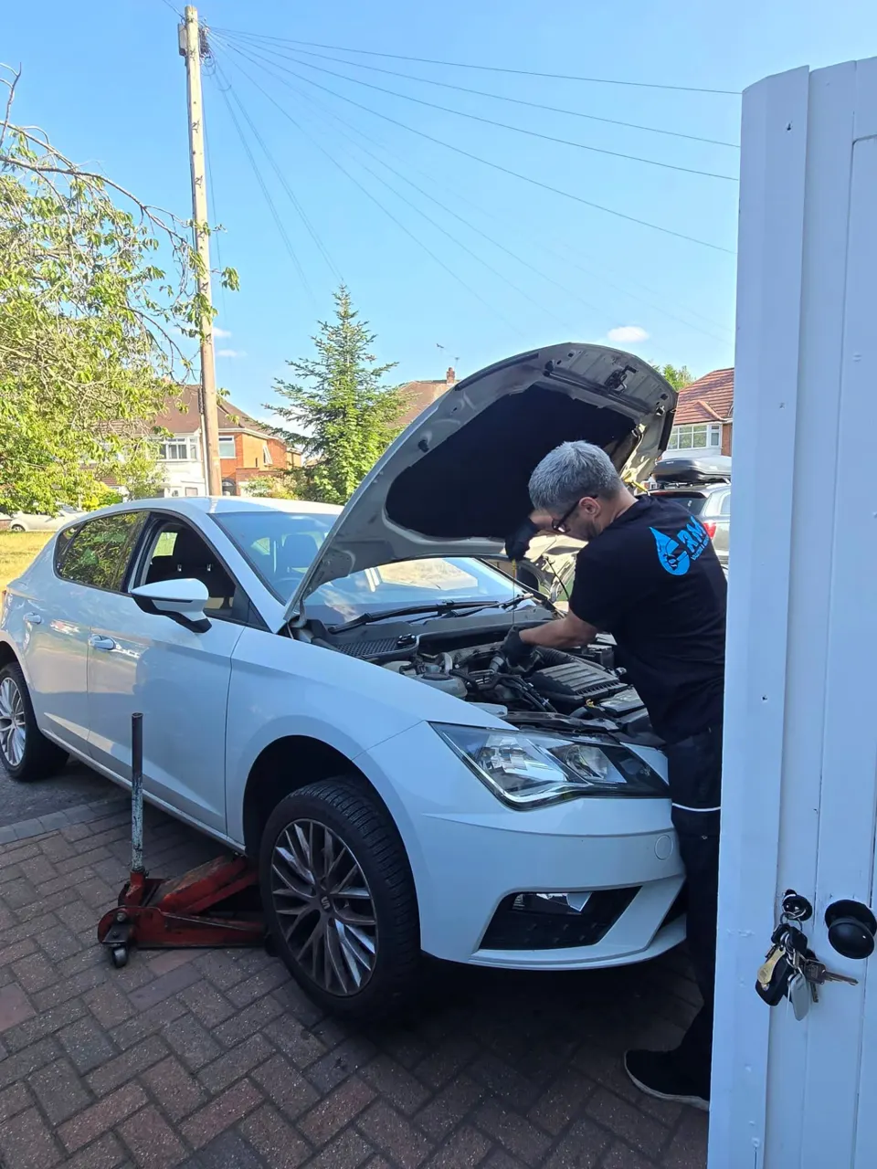 Riyaz working under the bonnet of a white Seat on a driveway