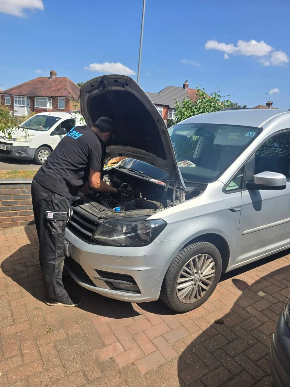 Riyaz working under the bonnet of a silver VW Caddy on a driveway