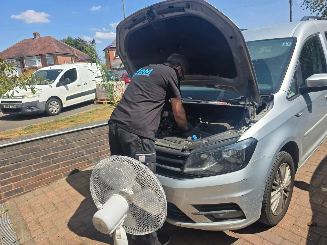 Riyaz replacing a glow plug on the VW Caddy with a fan beside him